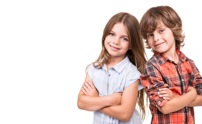 Two smiling children, a girl in a light blue blouse and a boy in a red plaid shirt, stand with arms crossed toward the camera.
